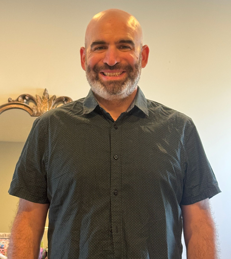 Man with short beard, smiling, wearing a grey polo shirt with a company logo.