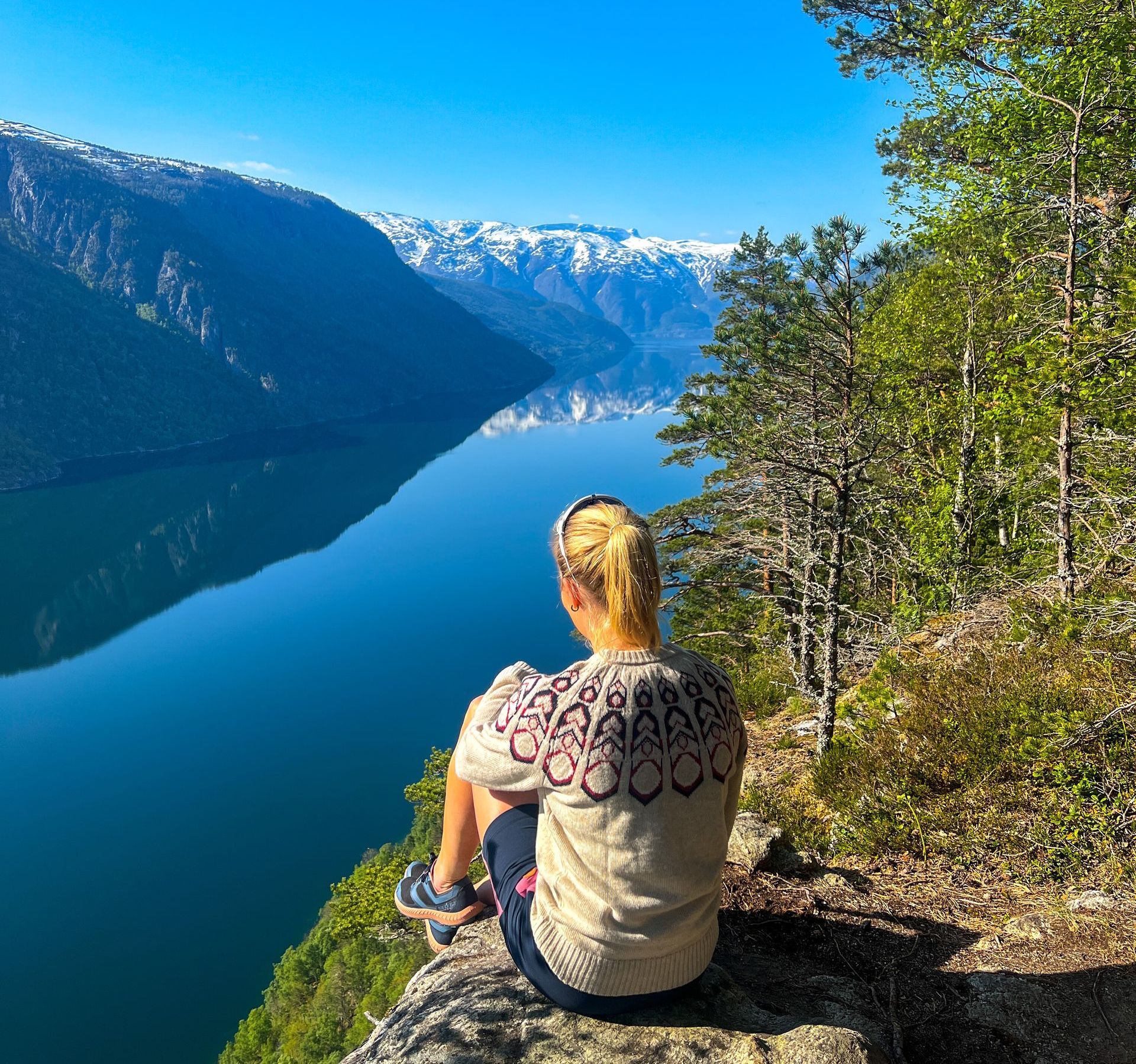 Woman sitting on rock, overlooking the Osafjord branch with mountains and snow.