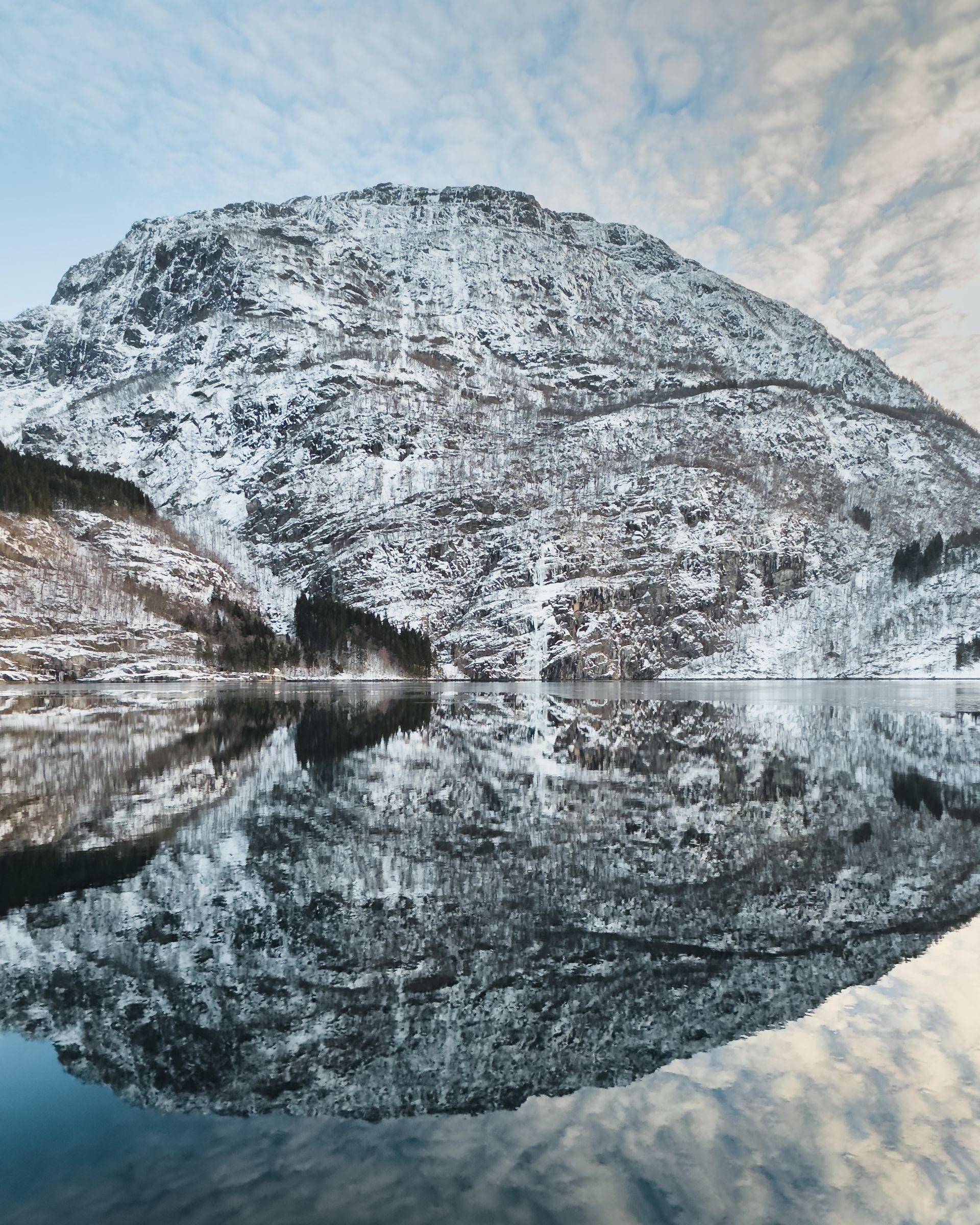 Snowy mountain reflected in calm fjord waters.