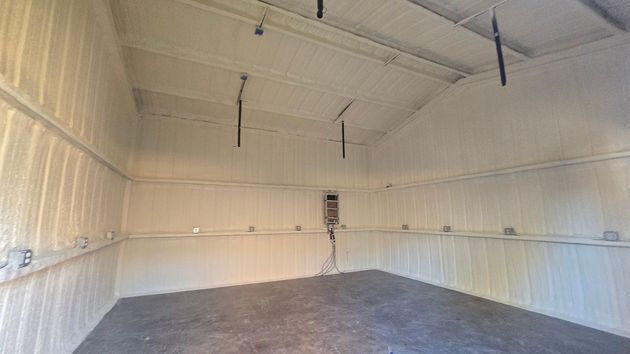 Empty white barn interior with a concrete floor and a ladder on the back wall.