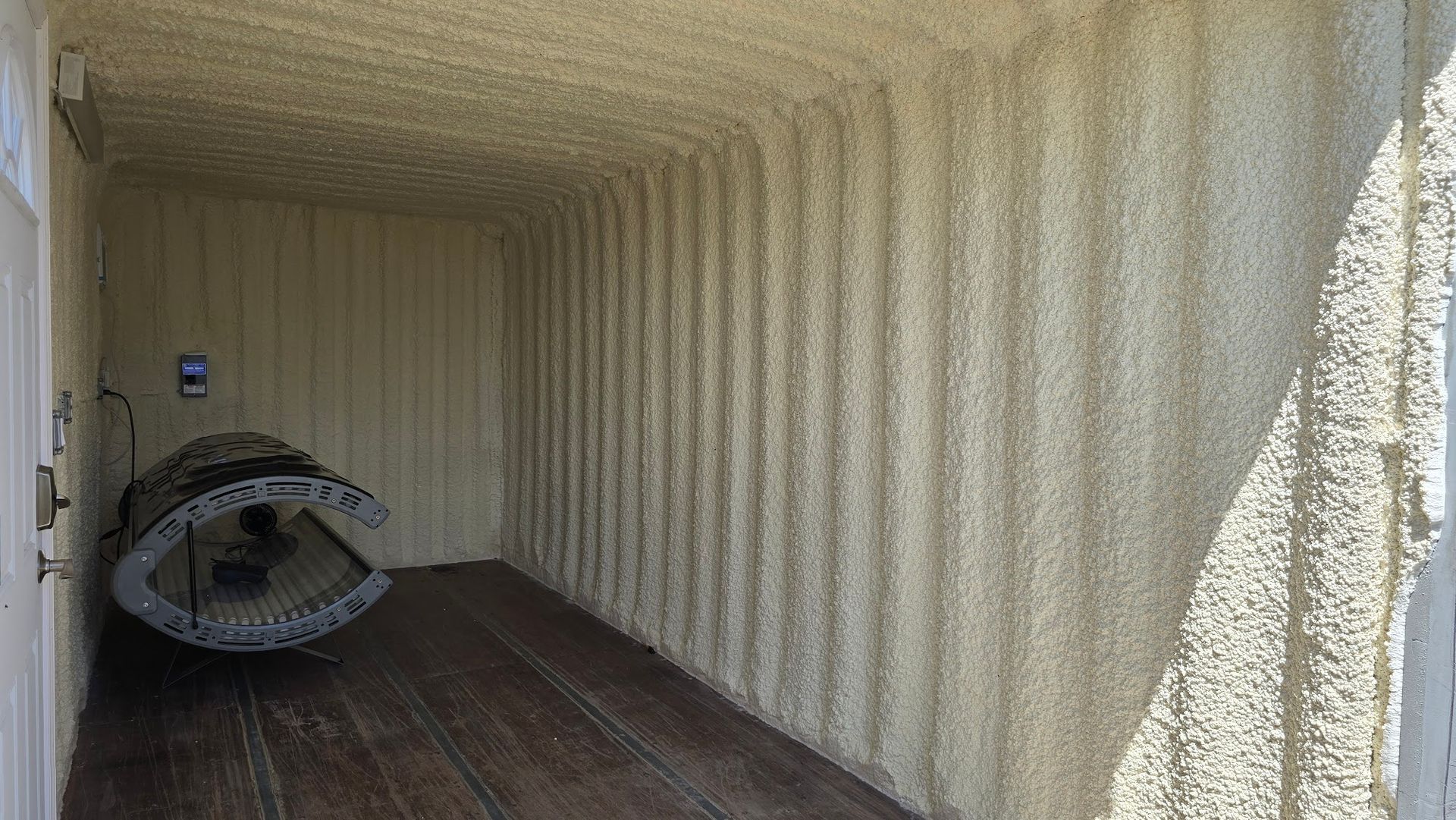 Empty shipping container with a hanging fan on the left and sunlight on the corrugated walls.