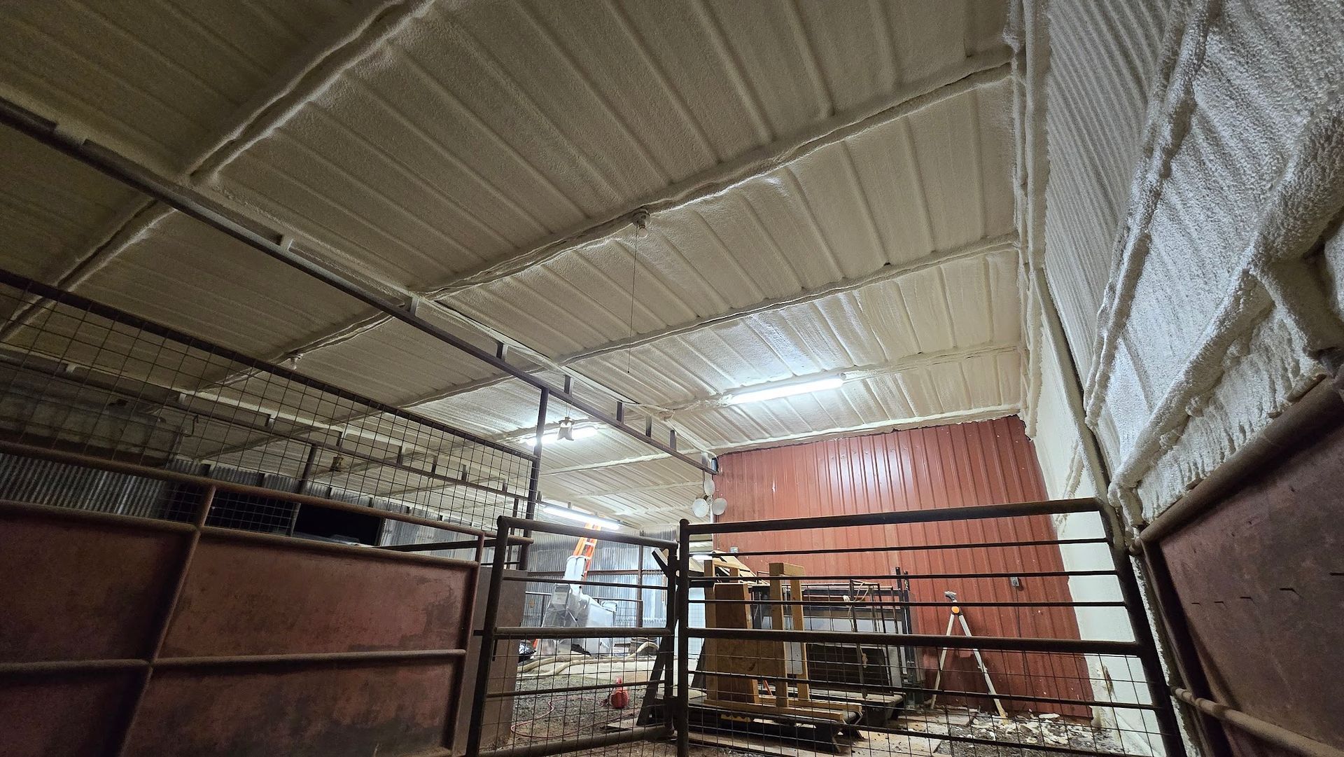 Covered livestock pen with metal fencing, red walls, and a corrugated roof inside a barn-like structure