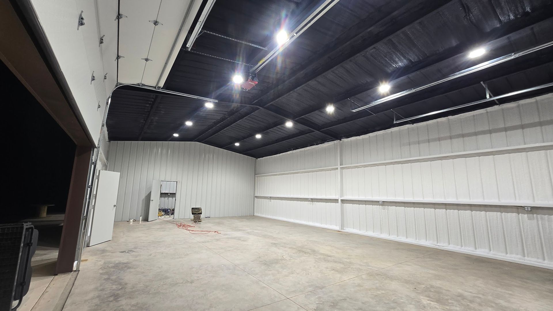 Empty warehouse interior with white walls, concrete floor, and black ceiling lights