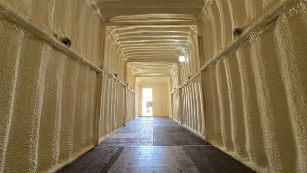 Empty wooden walkway with bright light at the far end, lined by textured walls and overhead beams.