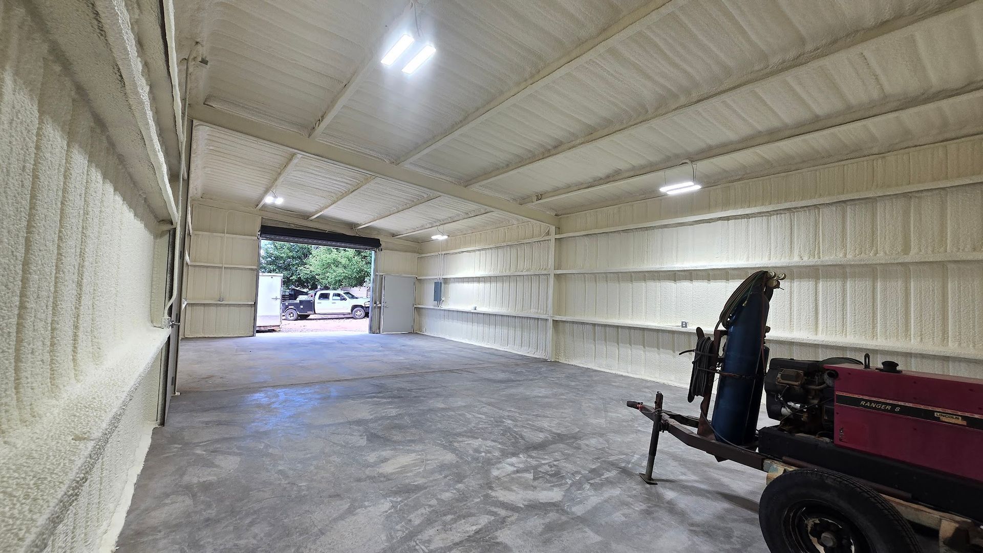 Empty beige garage or barn interior with concrete floor and a trailer on the right, open doorway ahead.