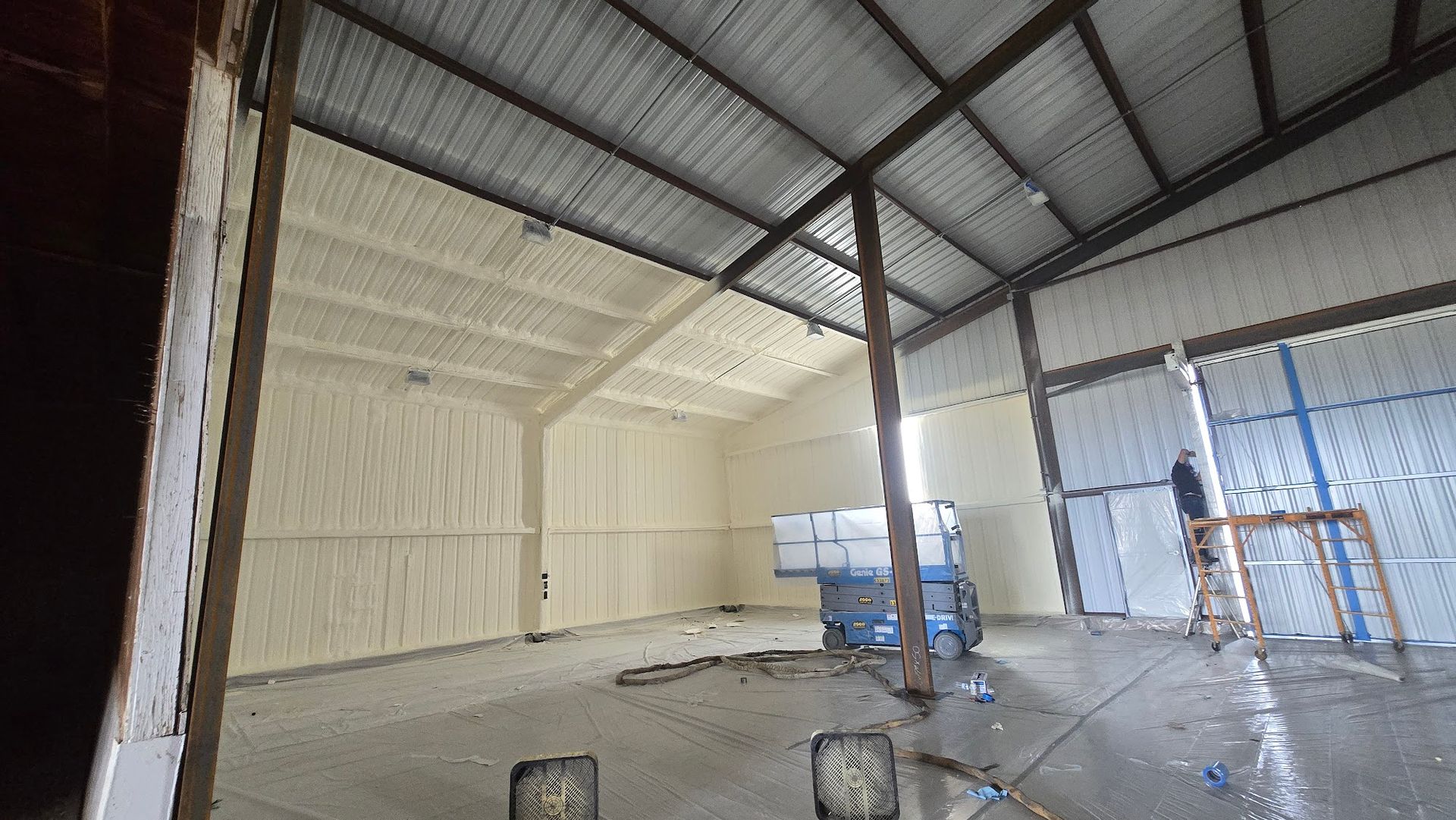 Empty metal warehouse interior with corrugated walls, concrete floor, and a blue lift near the center.