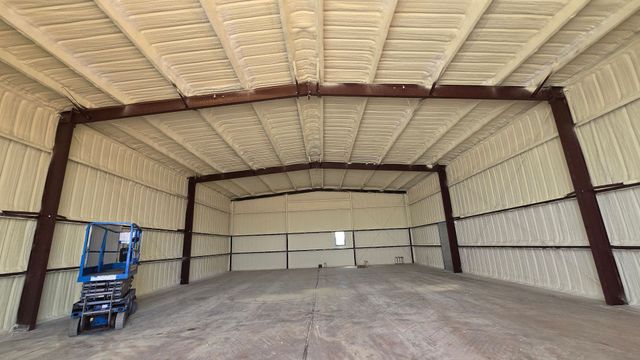 Empty warehouse interior with a blue scissor lift on the left and a large dirt mound in the center