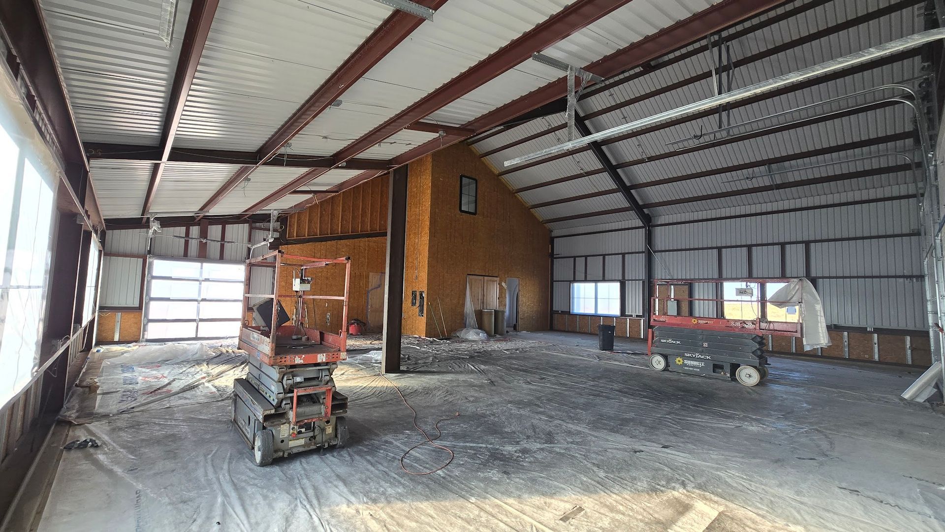 Interior of a large metal warehouse with a small wooden office, equipment, and unfinished concrete floor