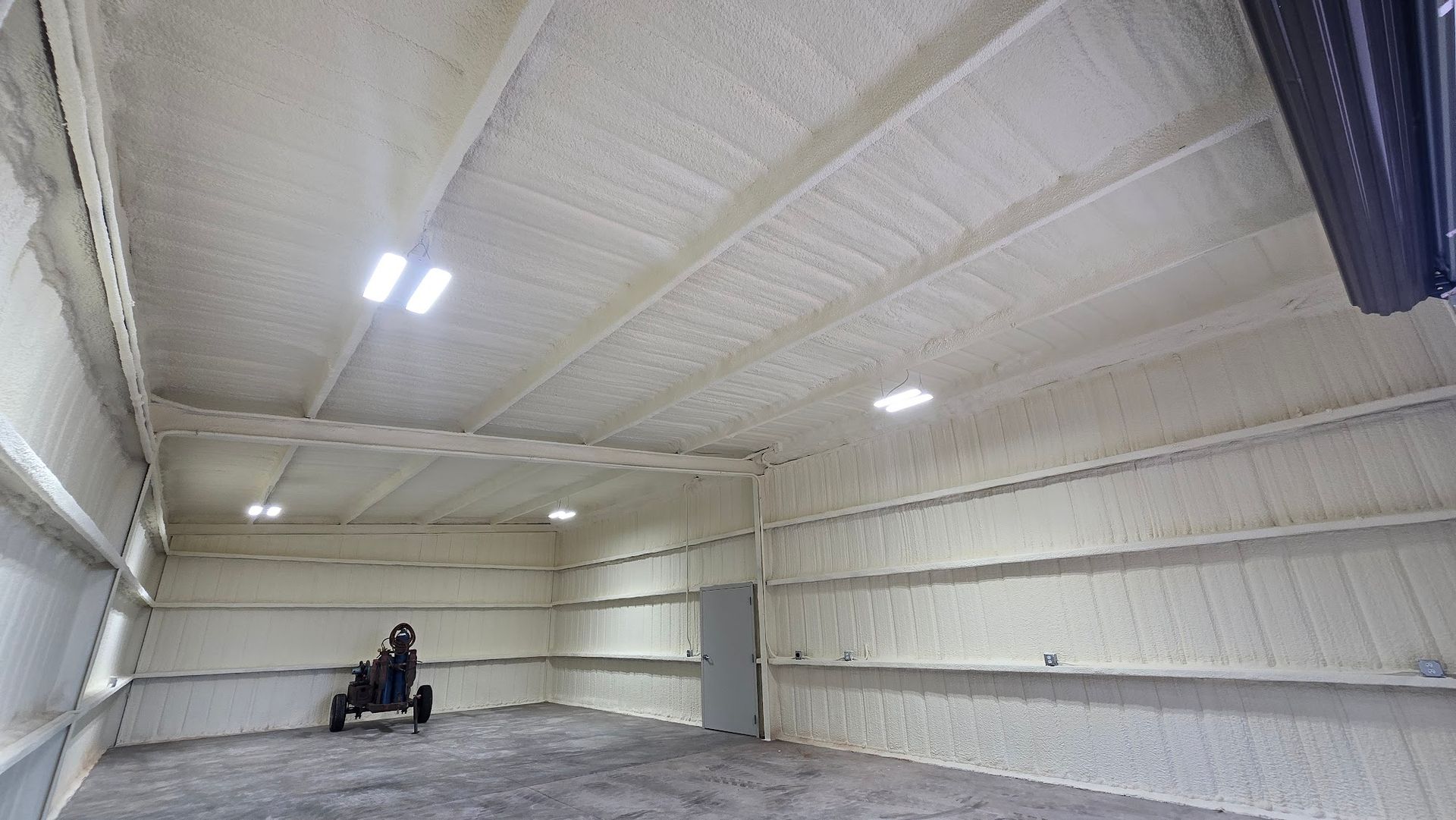 Large empty warehouse interior with white insulated walls, overhead lights, and a single chair near the back wall