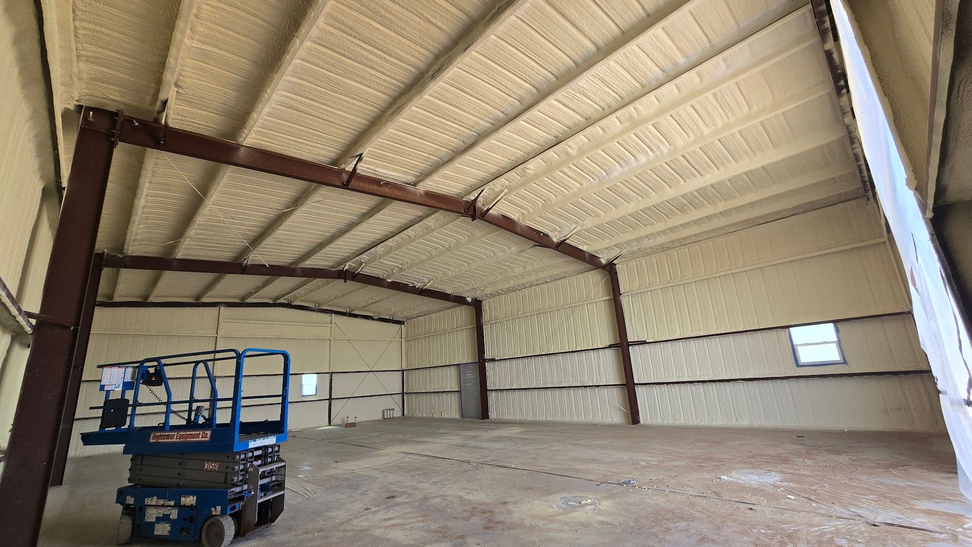 Empty warehouse interior with exposed steel beams and a blue lift parked on the left