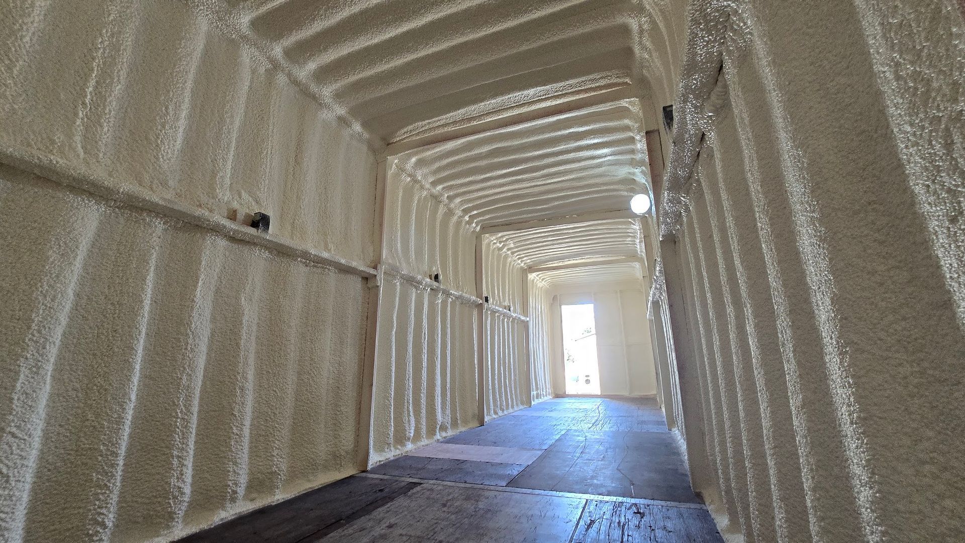 Insulated warehouse corridor with white foam walls and a bright opening at the end