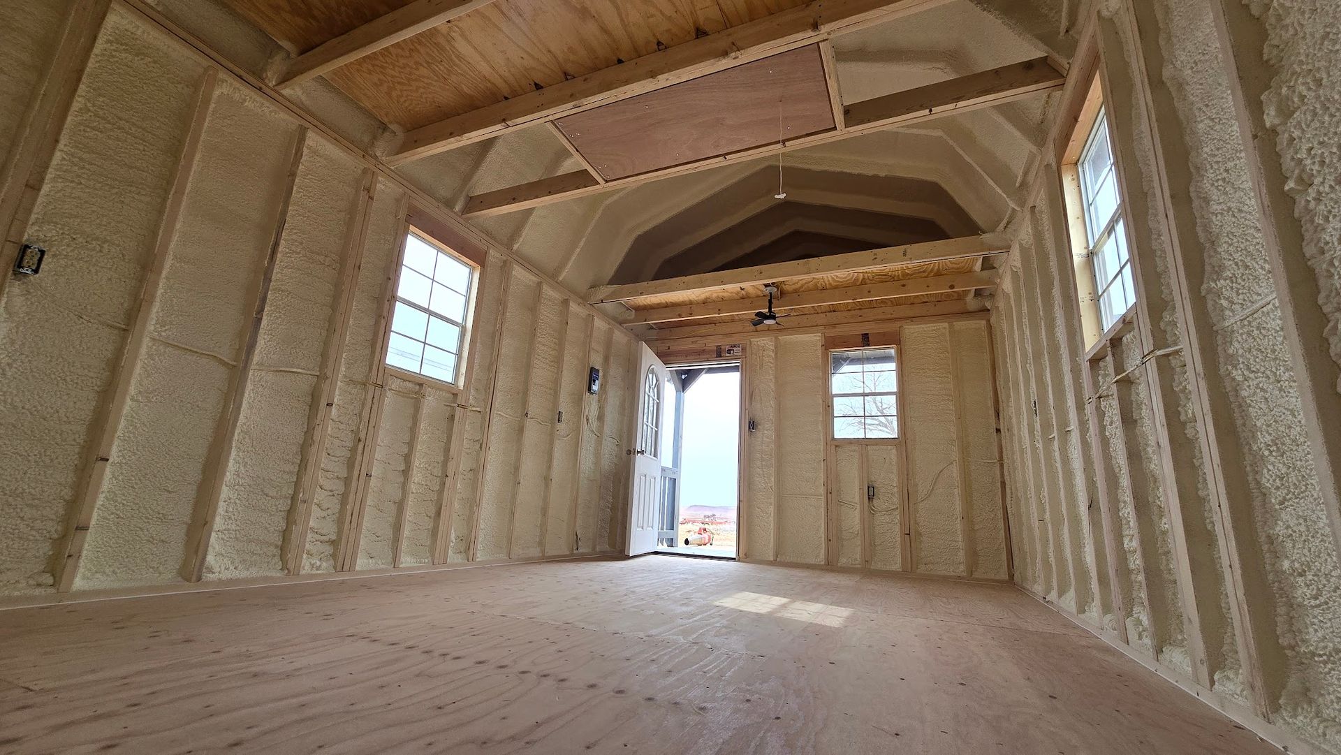 Empty unfinished wooden room with exposed framing, windows, and a doorway opening to daylight