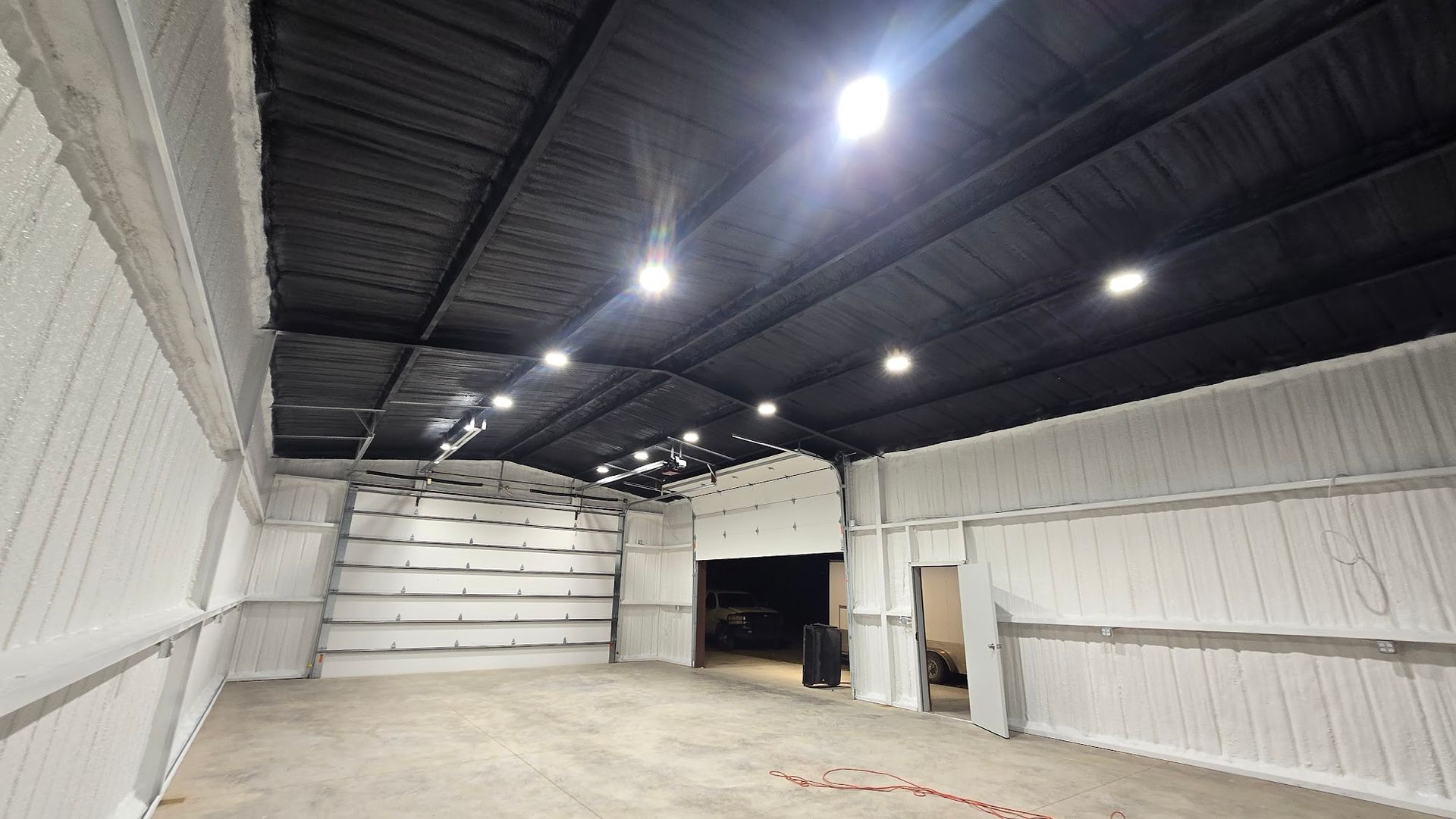 Empty warehouse interior with white walls, black ceiling, and bright overhead lights
