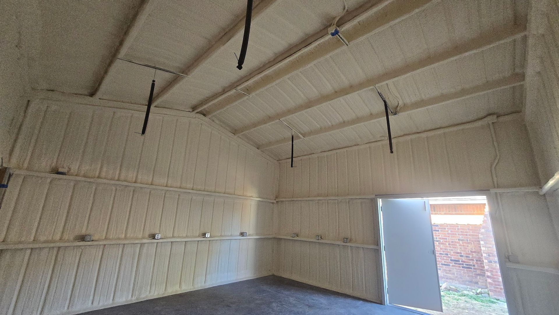 Empty insulated interior of a building with open doorway and exposed ceiling beams