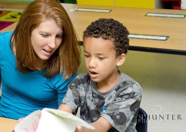 A Woman Is Reading a Book to A Young Boy in A Classroom.