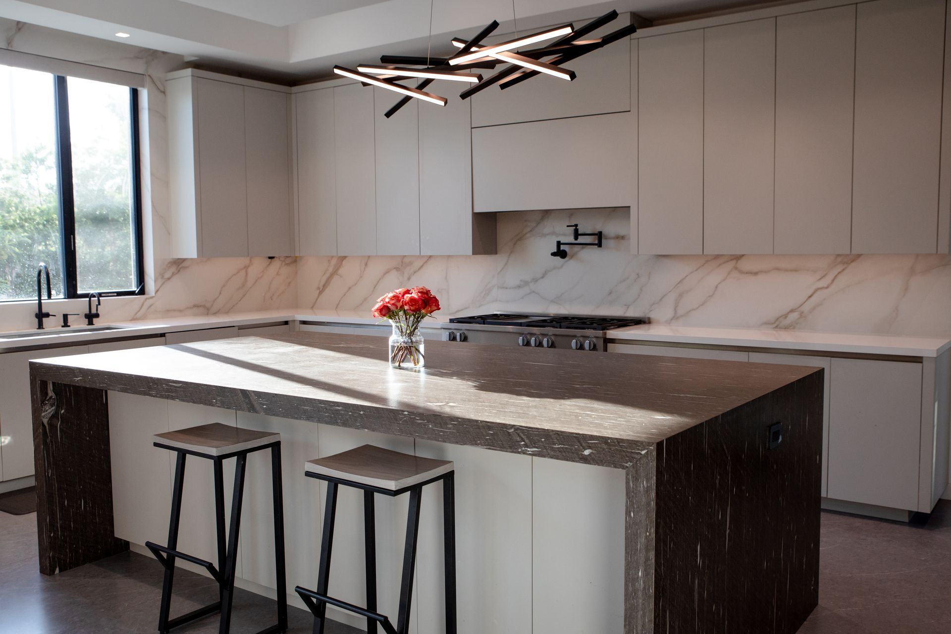 A kitchen with a large island and stools and a vase of flowers on the counter.