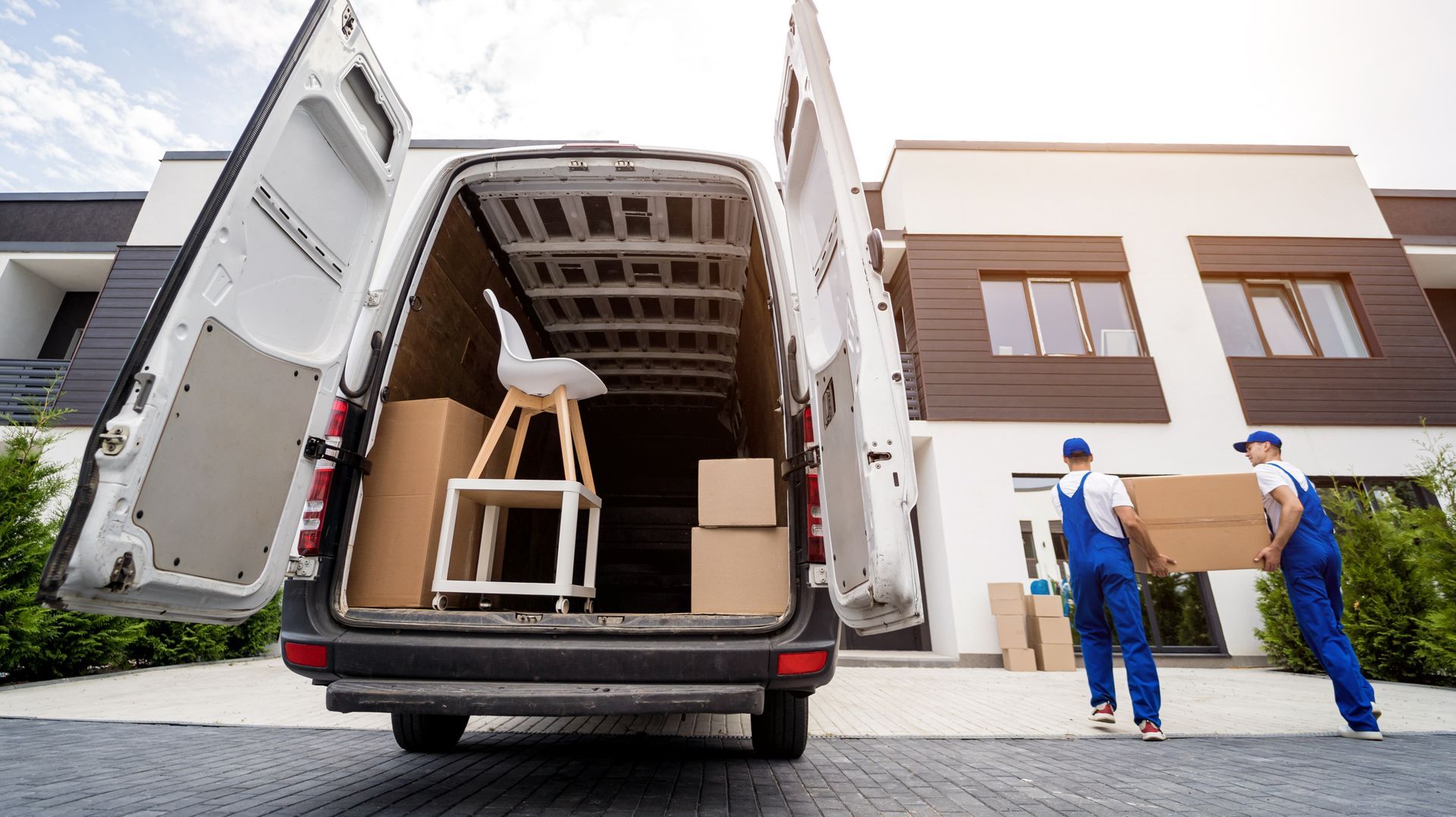 Two movers are performing moving services, unloading boxes and furniture from a minibus. Two movers are performing moving services, unloading boxes and furniture from a minibus.