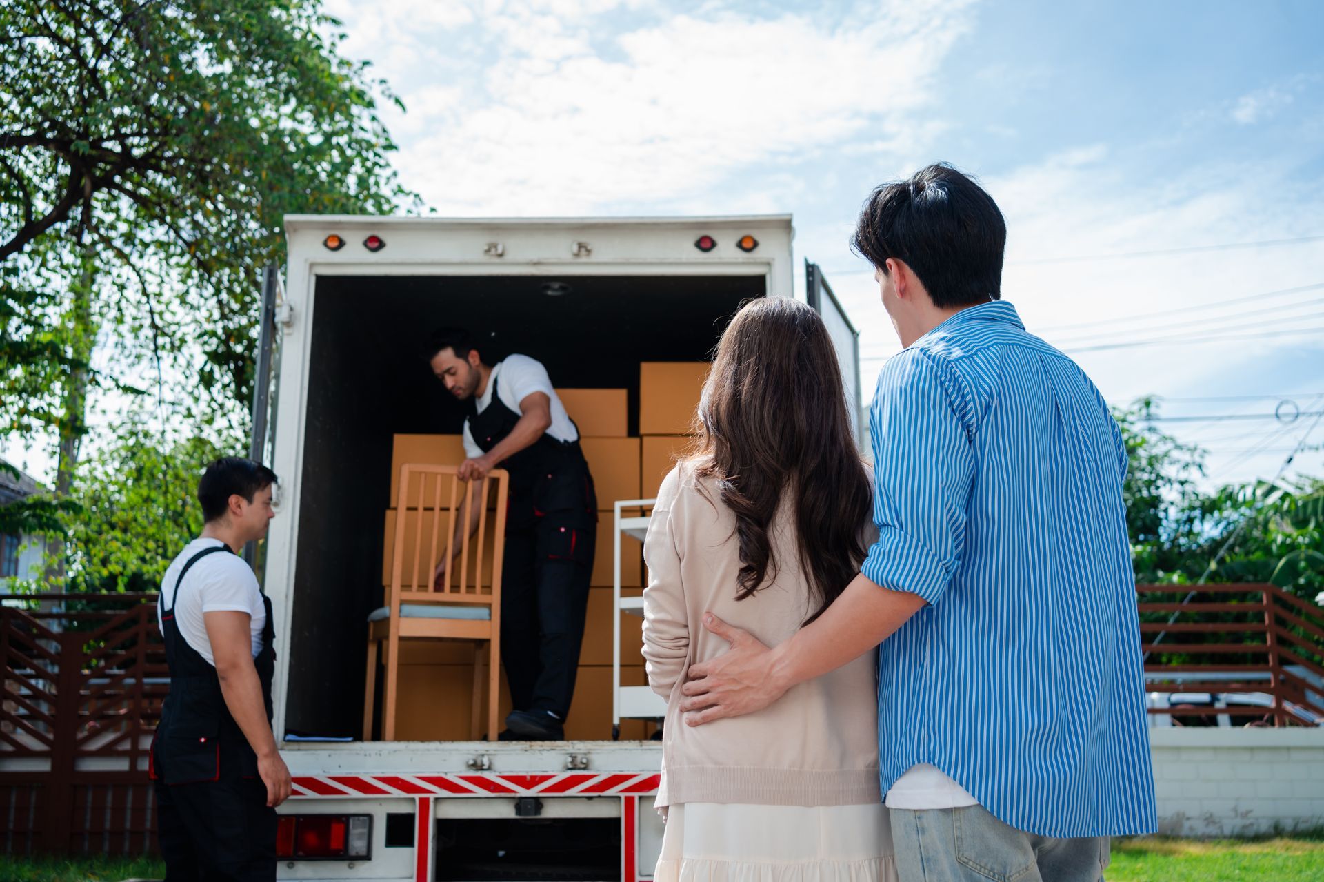 A couple checks the movers from the moving company, unload boxes and furniture from a truck. A couple checks the movers from the moving company, unload boxes and furniture from a truck.