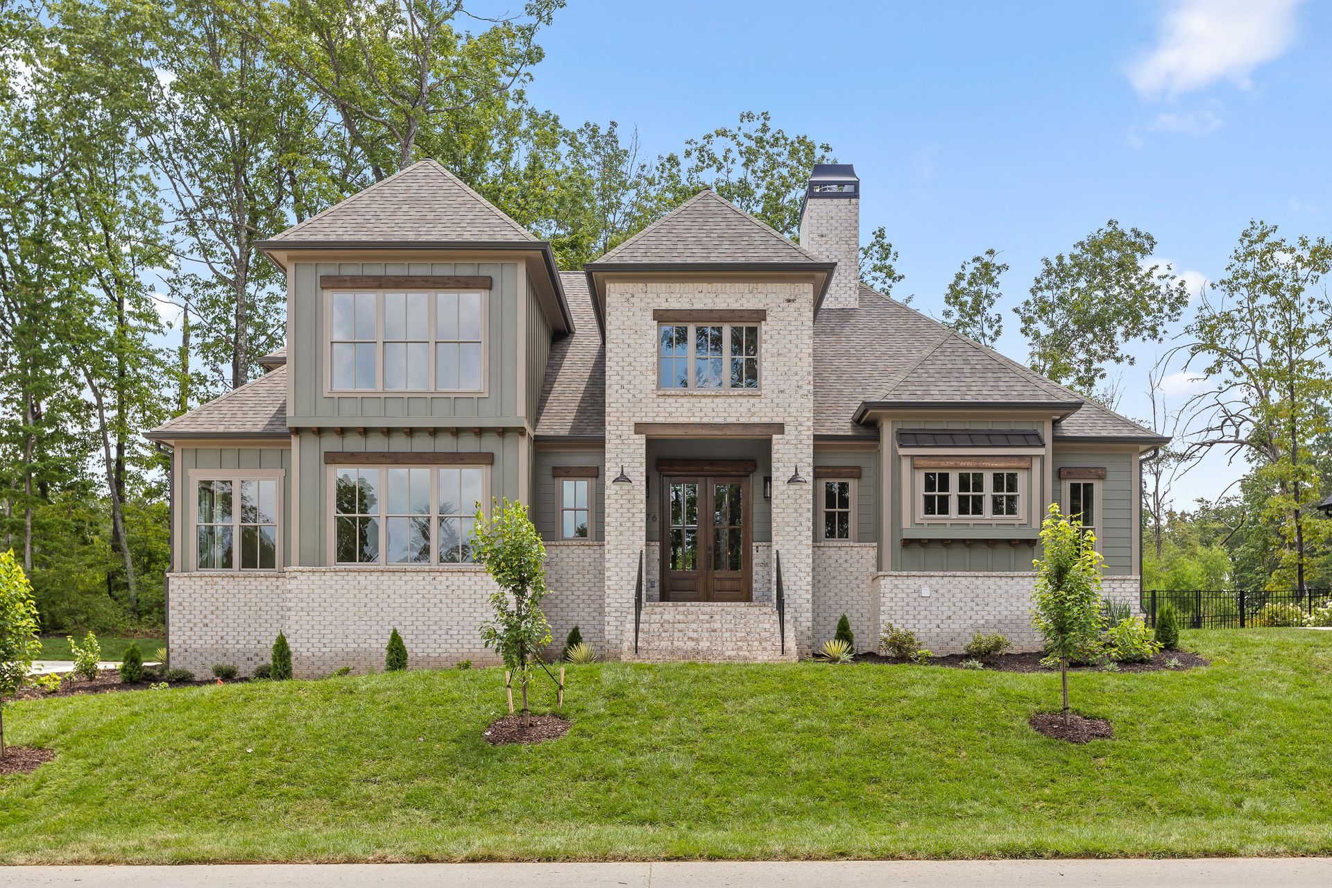 Modern two-story stone house with gray roof, large windows, and green lawn under a blue sky