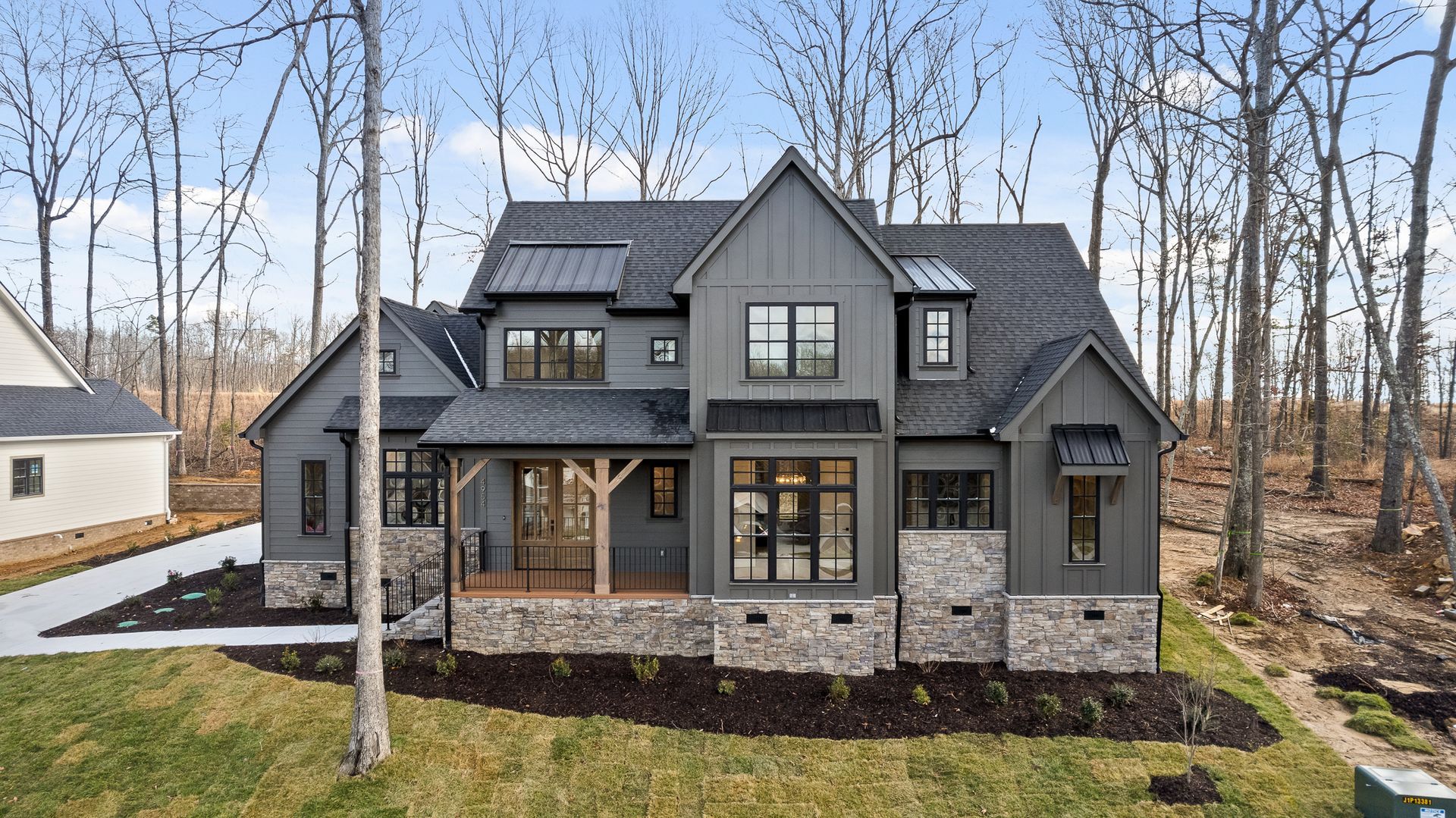 A custom home in Black Creek Chattanooga from NuHaven Homes that features a Modern gray two-story house with stone facade and large windows in a wooded setting