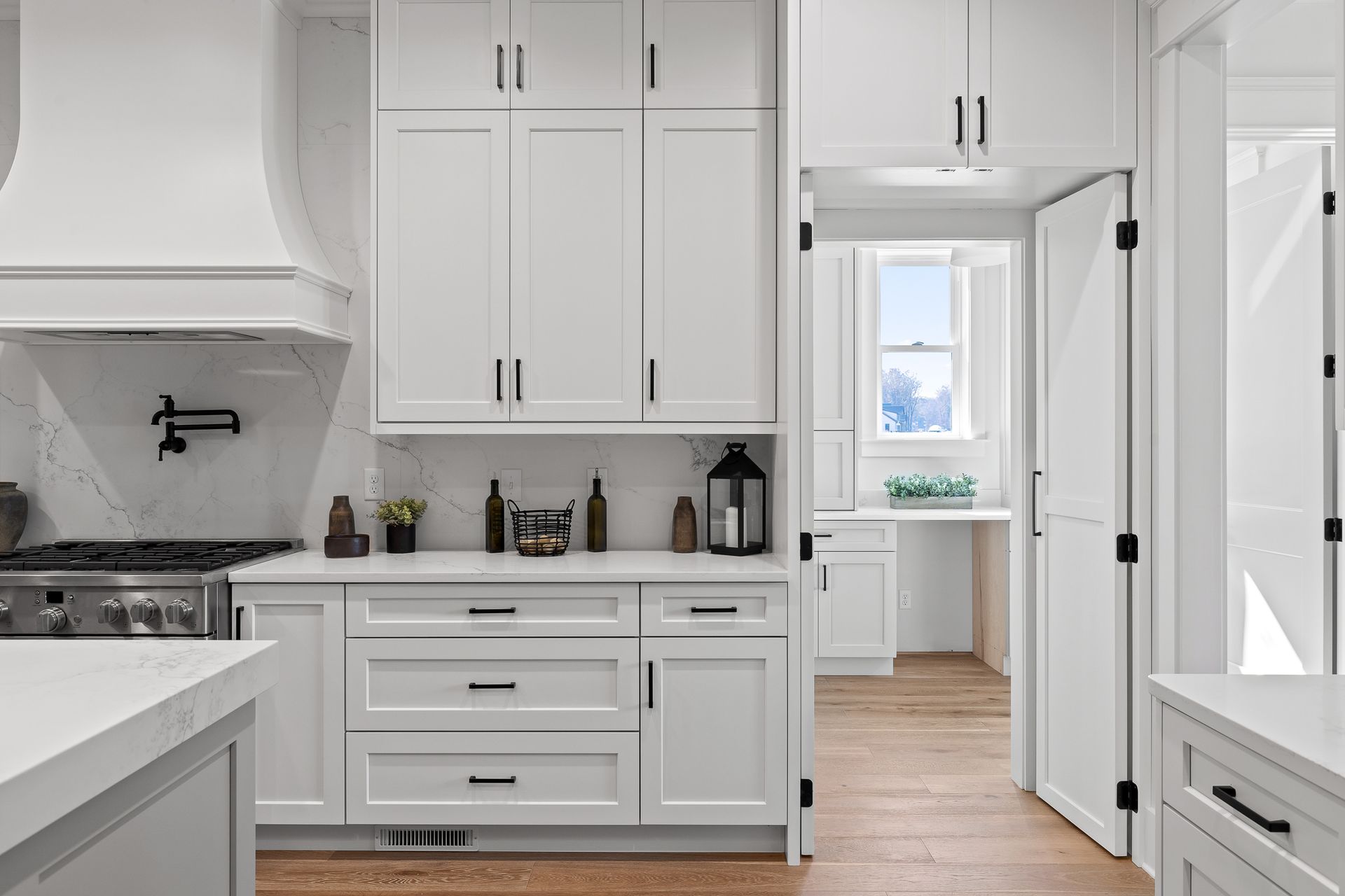 Bright white kitchen with cabinets, marble countertops, and a doorway to a sunlit pantry area
