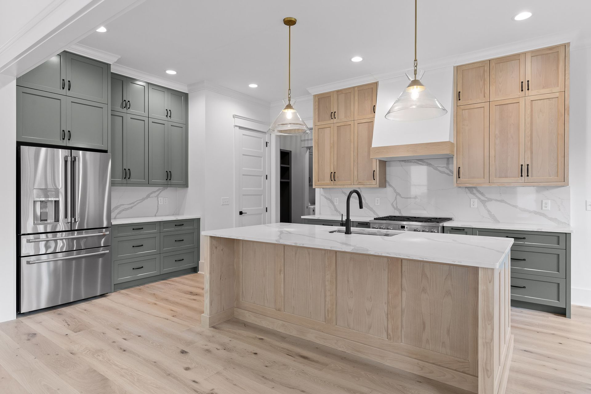 Modern kitchen with white marble island, light wood and gray cabinets, stainless steel fridge, and pendant lights