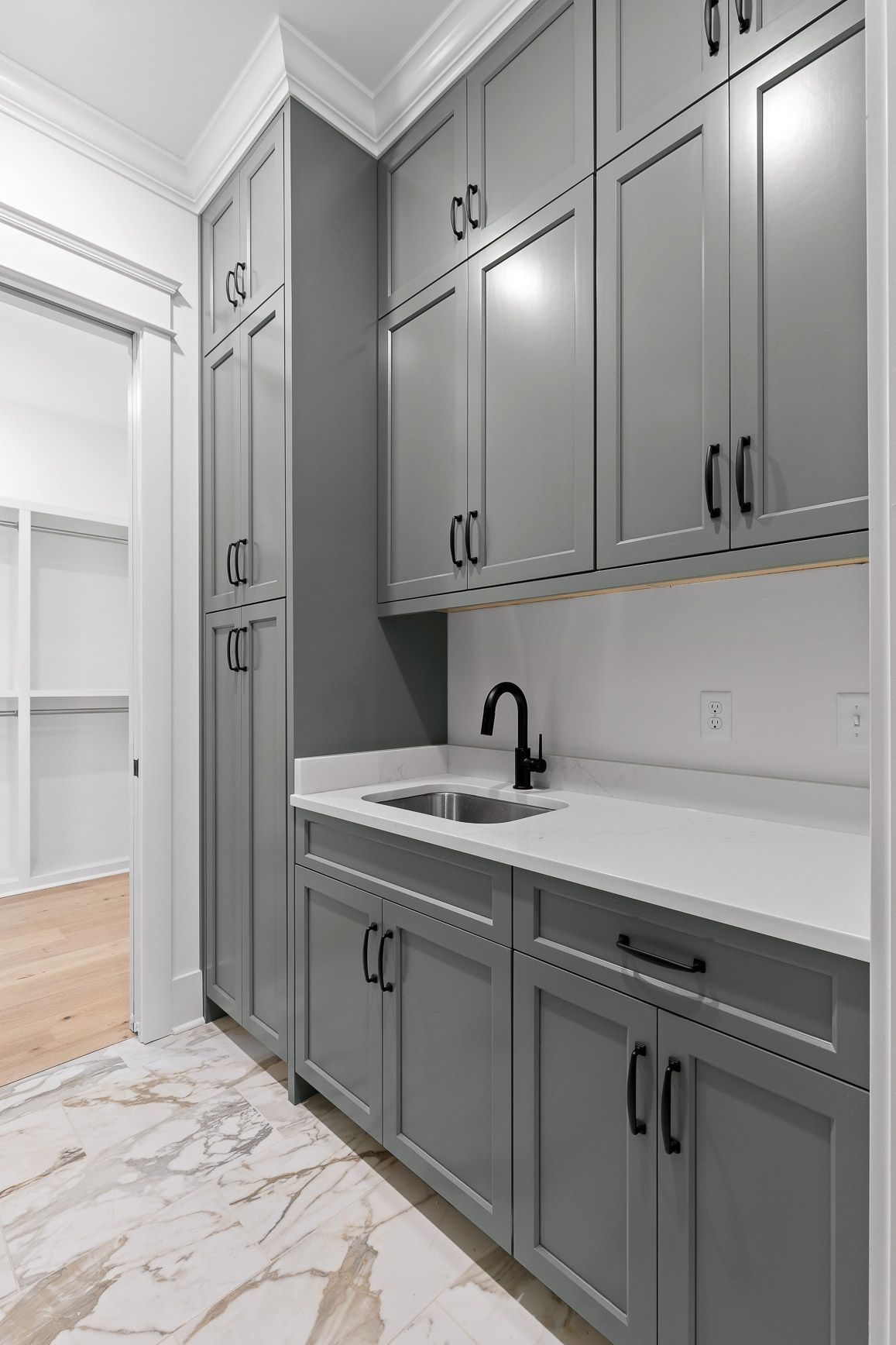 Modern kitchen with gray cabinets, white countertops, sink, and marble-look tile floor.