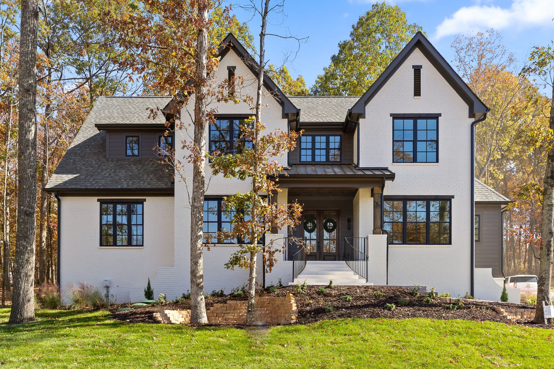 A custom built home in Black Creek Chattanooga that features a Large white two-story house with dark trim and gabled roof, surrounded by trees and green lawn
