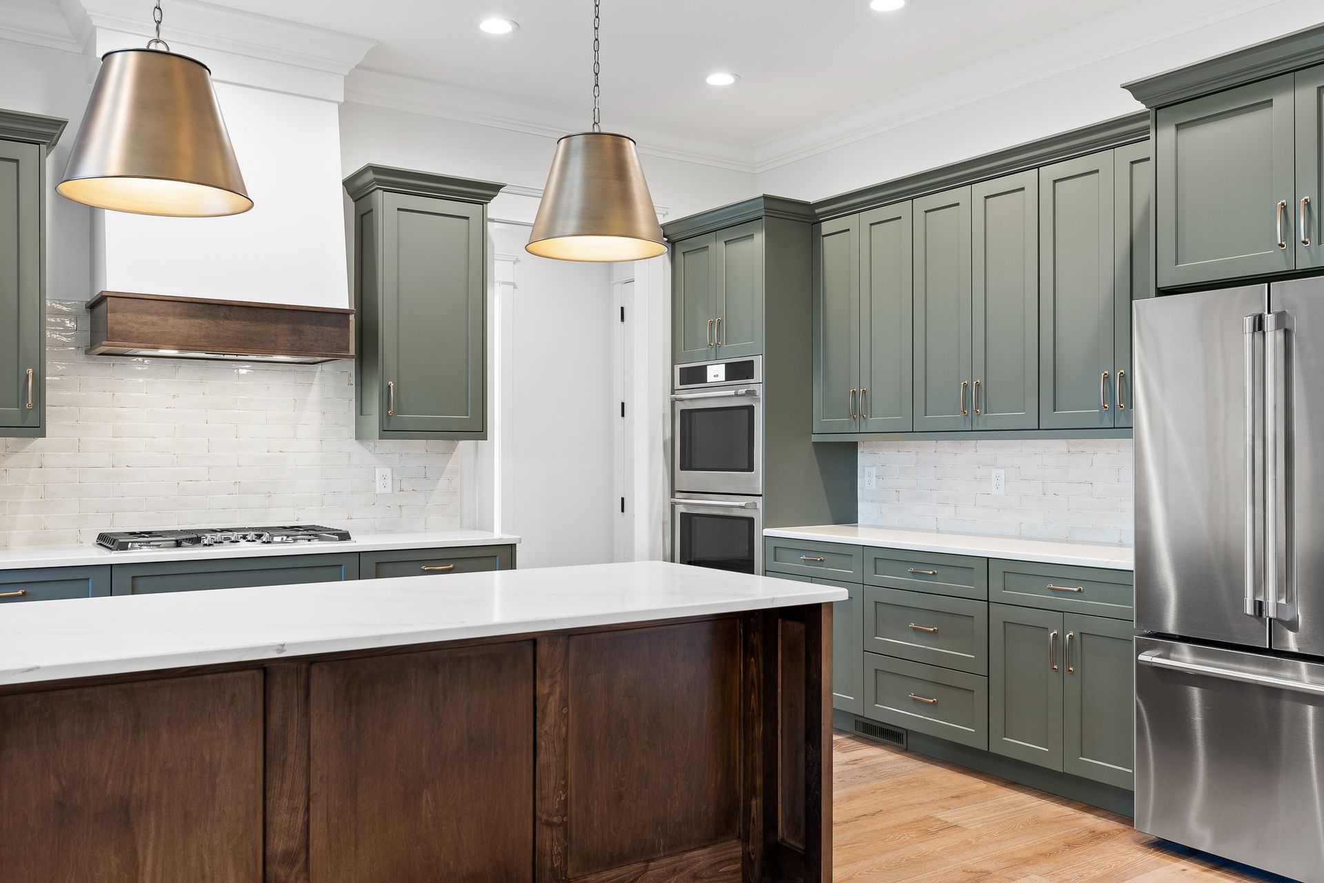 Modern kitchen with sage cabinets, stainless steel appliances, white island, and pendant lights