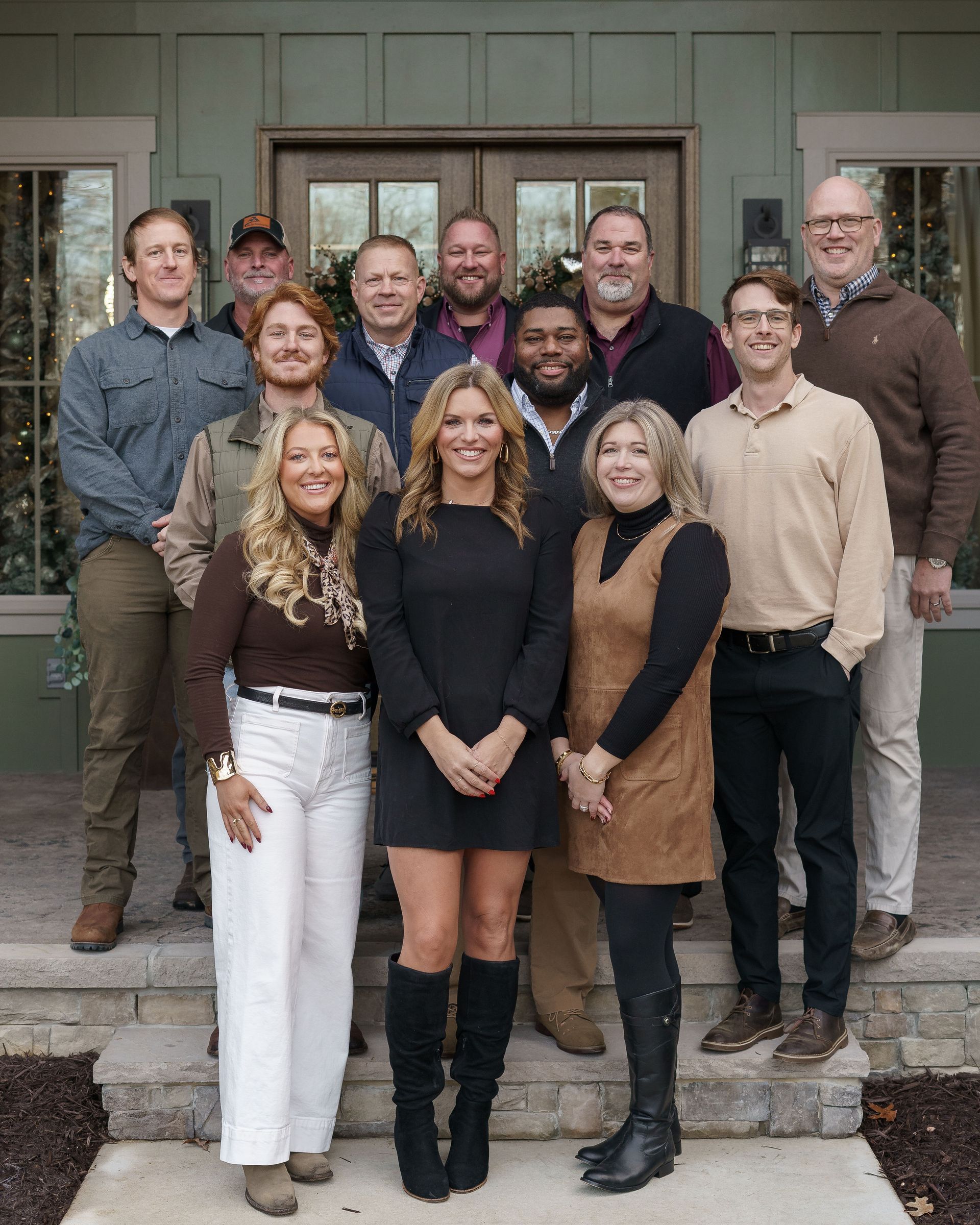 Group of people posing on outdoor steps in front of a building entrance, smiling at the camera.