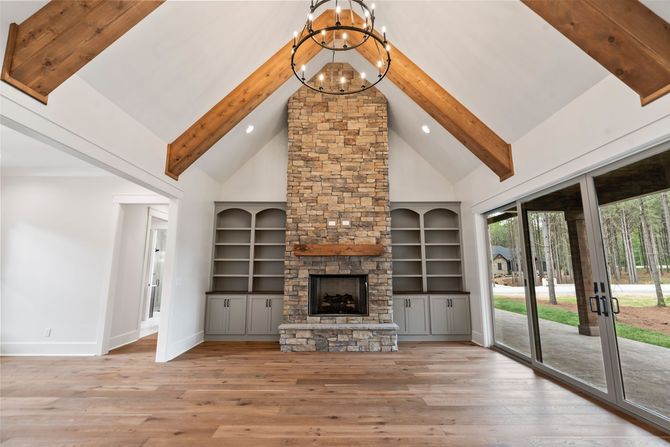 Spacious living room with vaulted wood ceiling, stone fireplace, built-in shelves, and large windows.