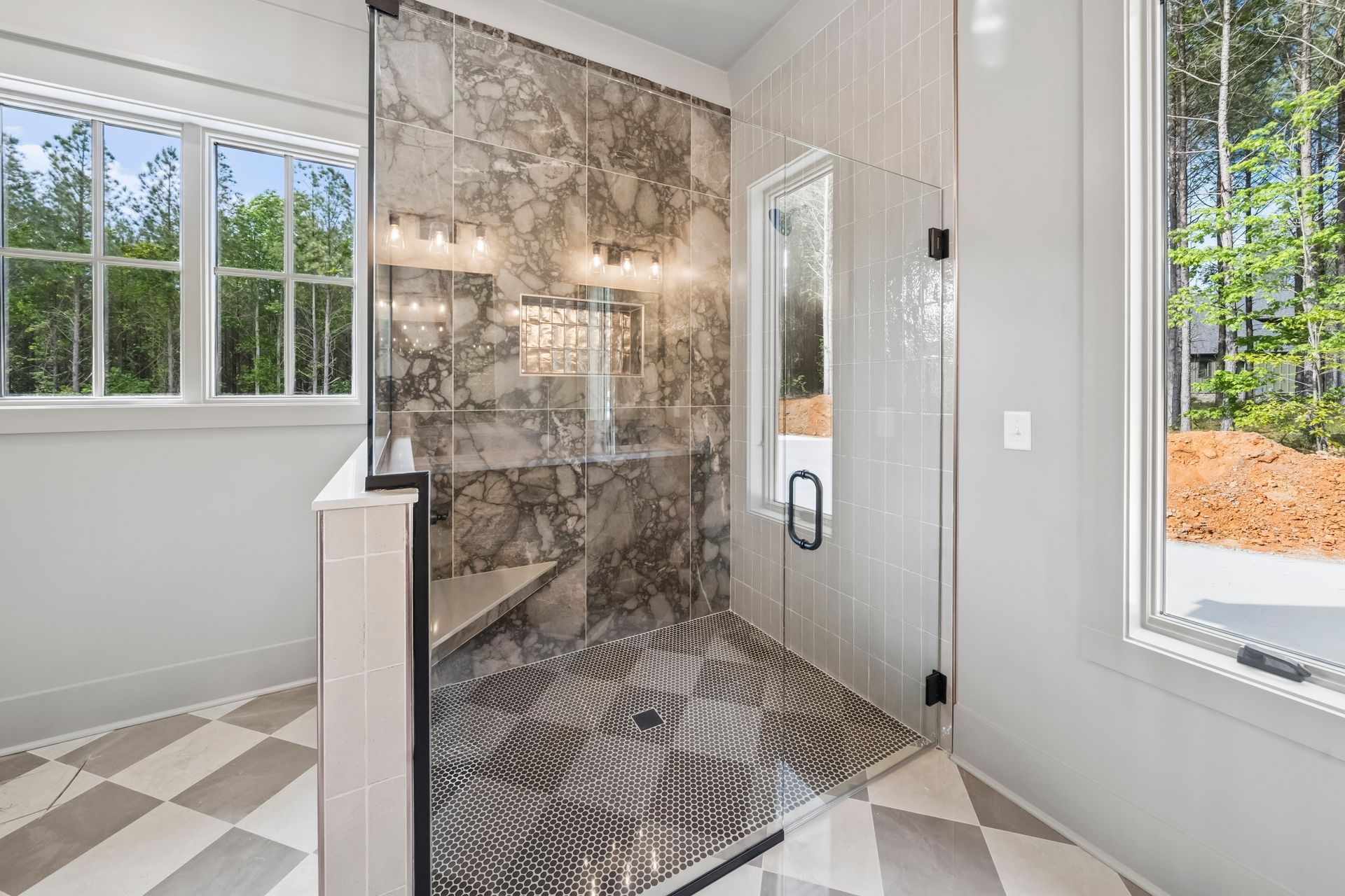 Modern bathroom with glass walk-in shower, patterned tile floor, and large windows