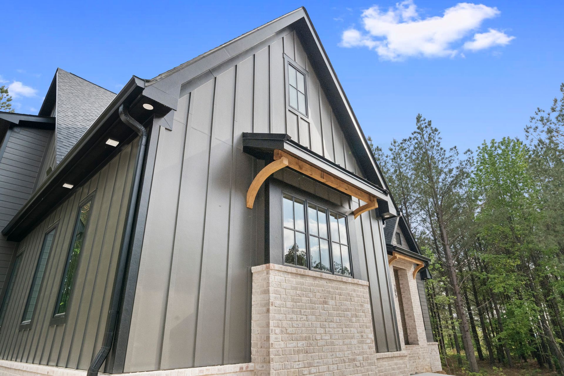 Modern gray house exterior with steep gabled roof, black-trimmed windows, and stone base under a blue sky