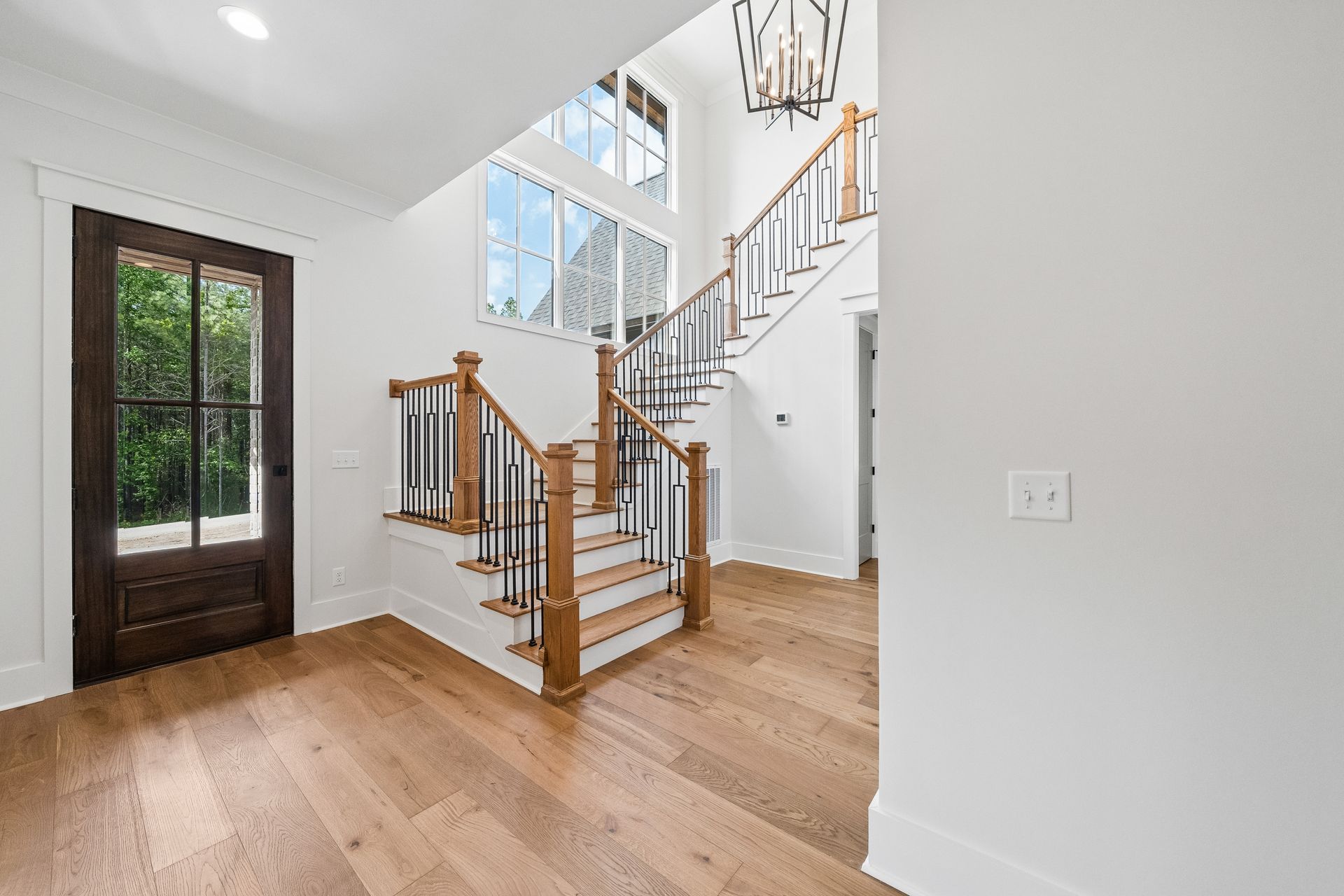 Bright entryway with hardwood floors, staircase, and large windows; dark front door on the left.