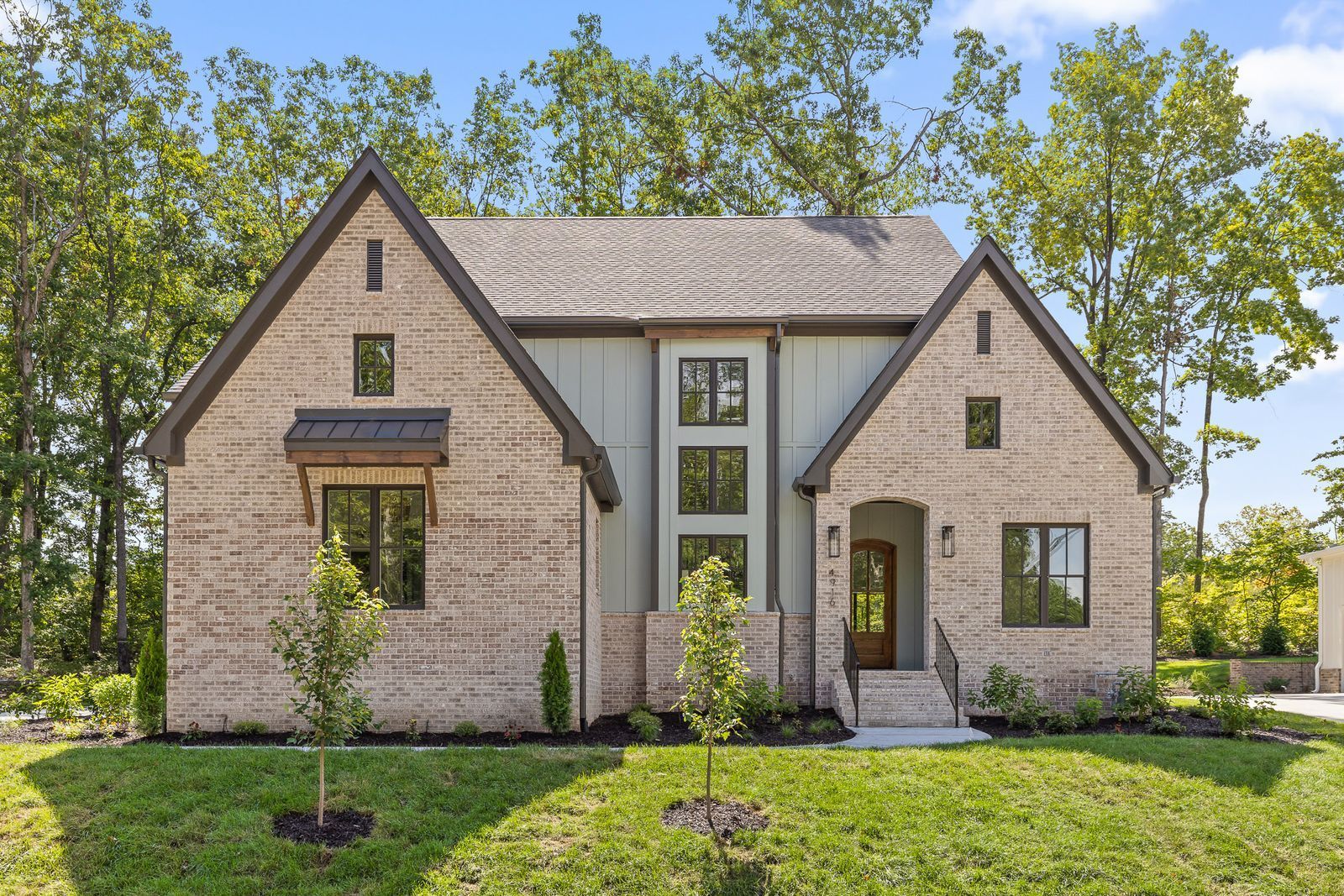 Modern brick house with gabled roofs, large windows, and a landscaped front yard under trees.