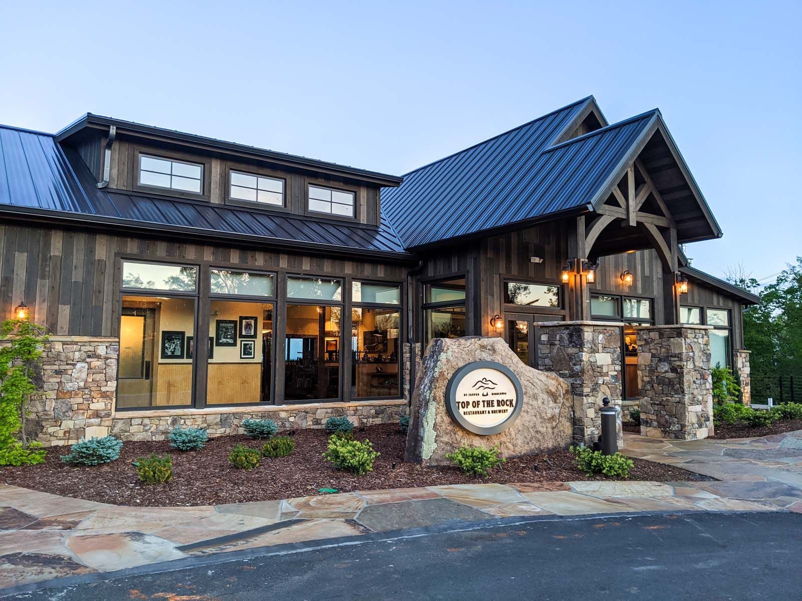 Top of the Rock Restaurant in Jasper Highlands Rustic stone-and-wood restaurant exterior with blue metal roof and lit windows at dusk