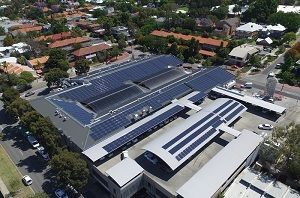 Aerial view of a large building with solar panels on the roof. Houses and trees surround the building.