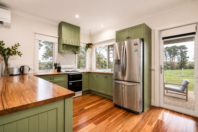 Modern kitchen with green cabinets, stainless steel fridge, wood countertops, and large windows.