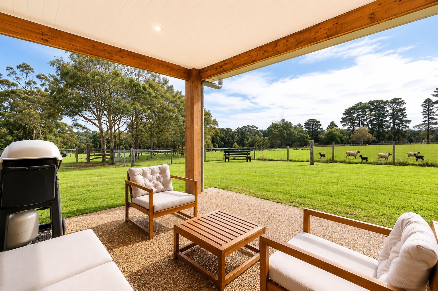 Covered patio overlooking a green field, with wicker chairs, a small table, and a grill.