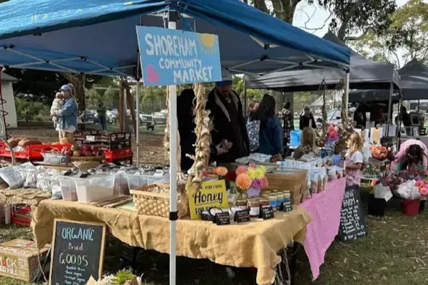 Outdoor market stall under blue canopy with handmade crafts, signs, and flowers on display