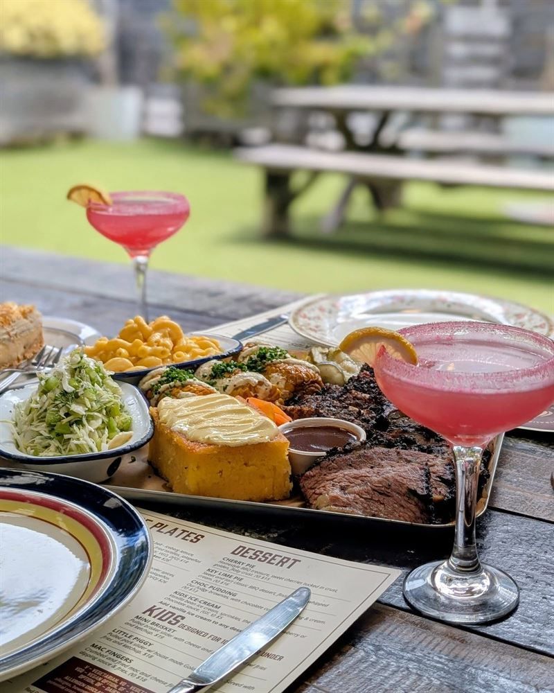 Outdoor picnic table with plated meal, pink cocktails, and a picnic basket in a grassy park