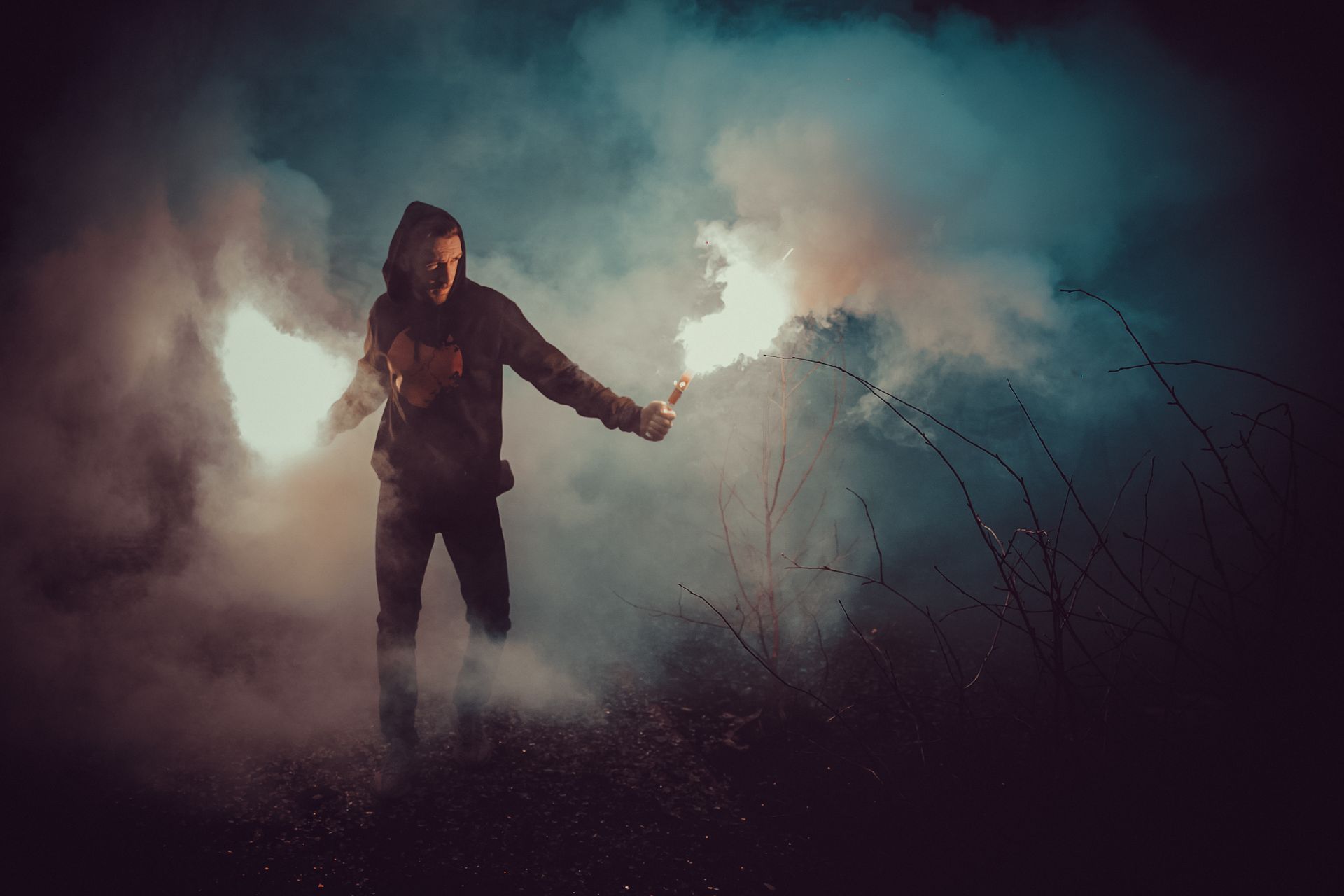Person in a dark hoodie walking through red smoke