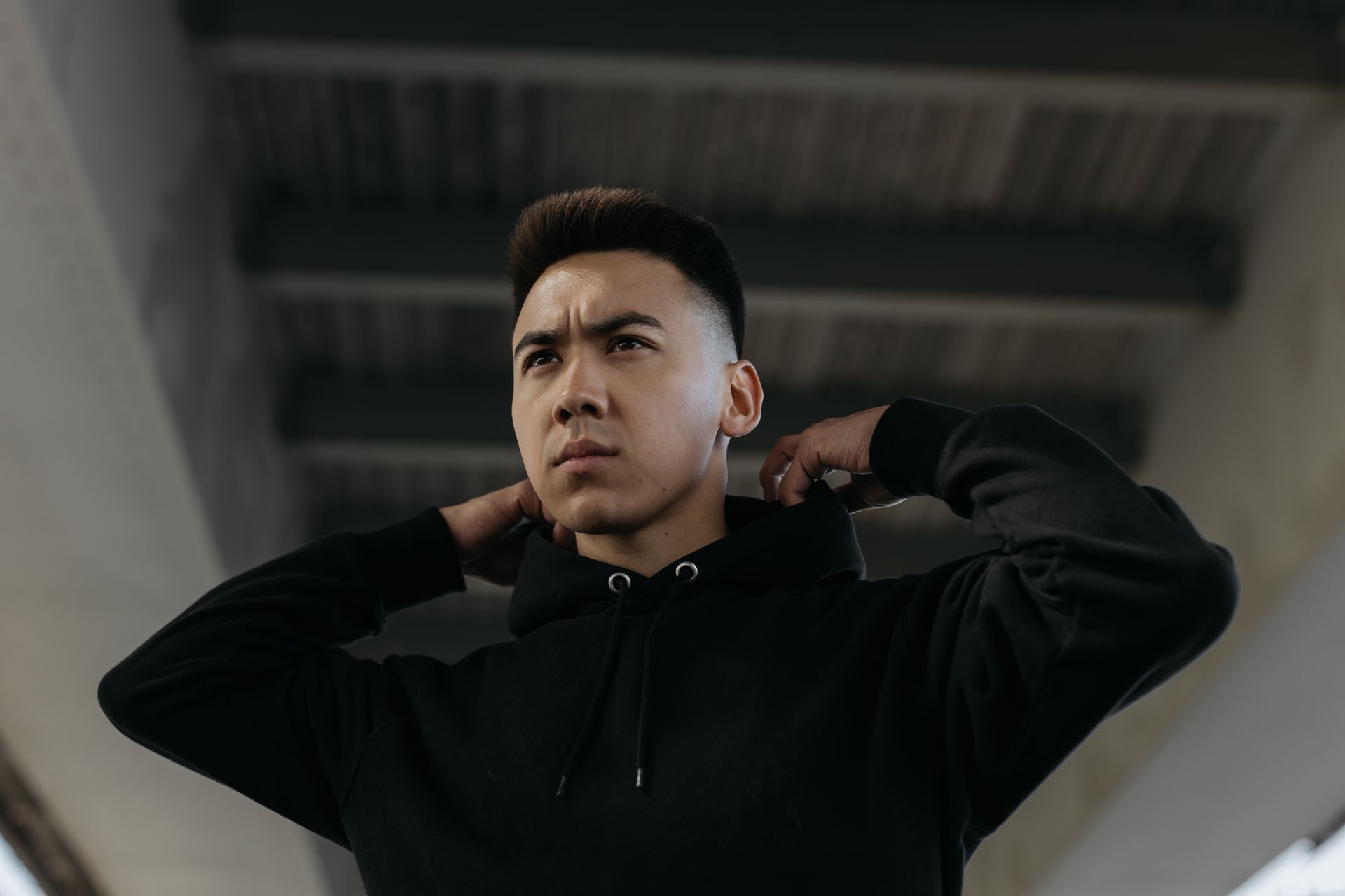Young man in a black hoodie standing under a bridge