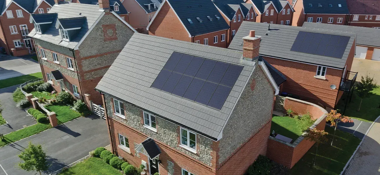Houses with solar panels on the roofs. Brick and gray stone facade with green lawns.