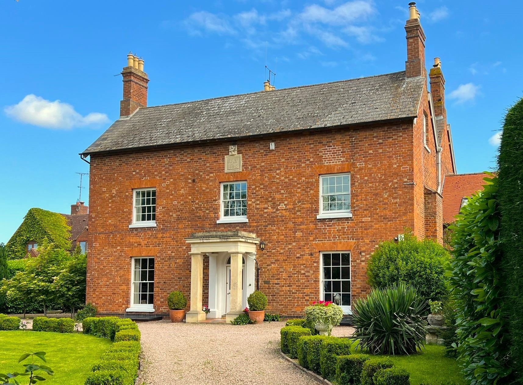 Brick house with white windows and a small portico entrance under a bright blue sky.