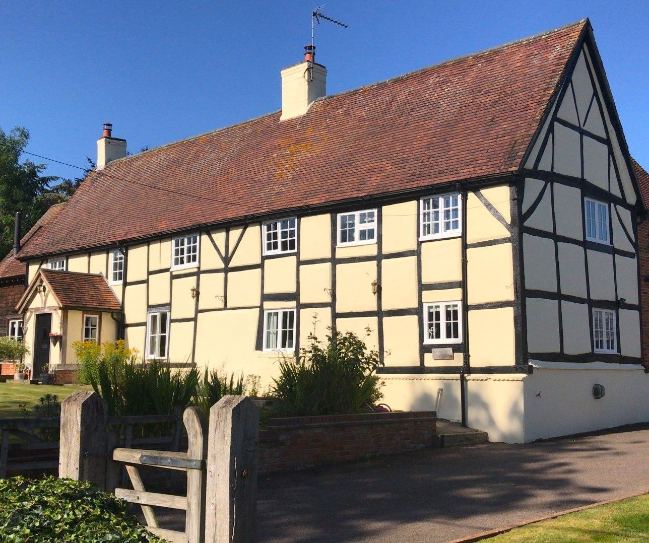 Two-story Tudor-style house with beige walls, black beams, red roof, and small white windows.
