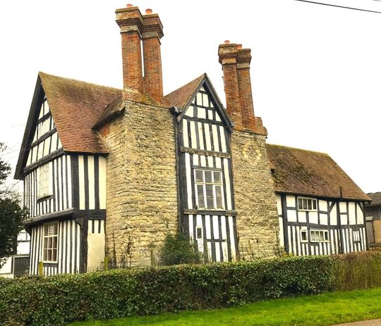 Tudor style house with black beams, stone walls, and red tile roof. Two brick chimneys.