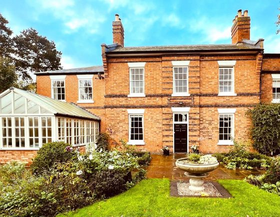A brick mansion with a conservatory and a garden, overcast sky.