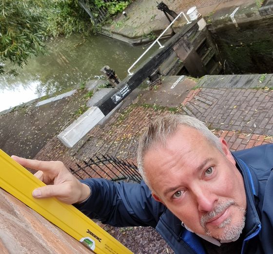 Man using level on brick wall by canal lock.