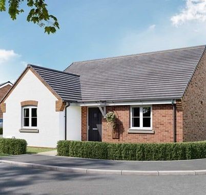 Bungalow with white stucco and red brick exterior. Gray roof, black door. Green hedge in front.